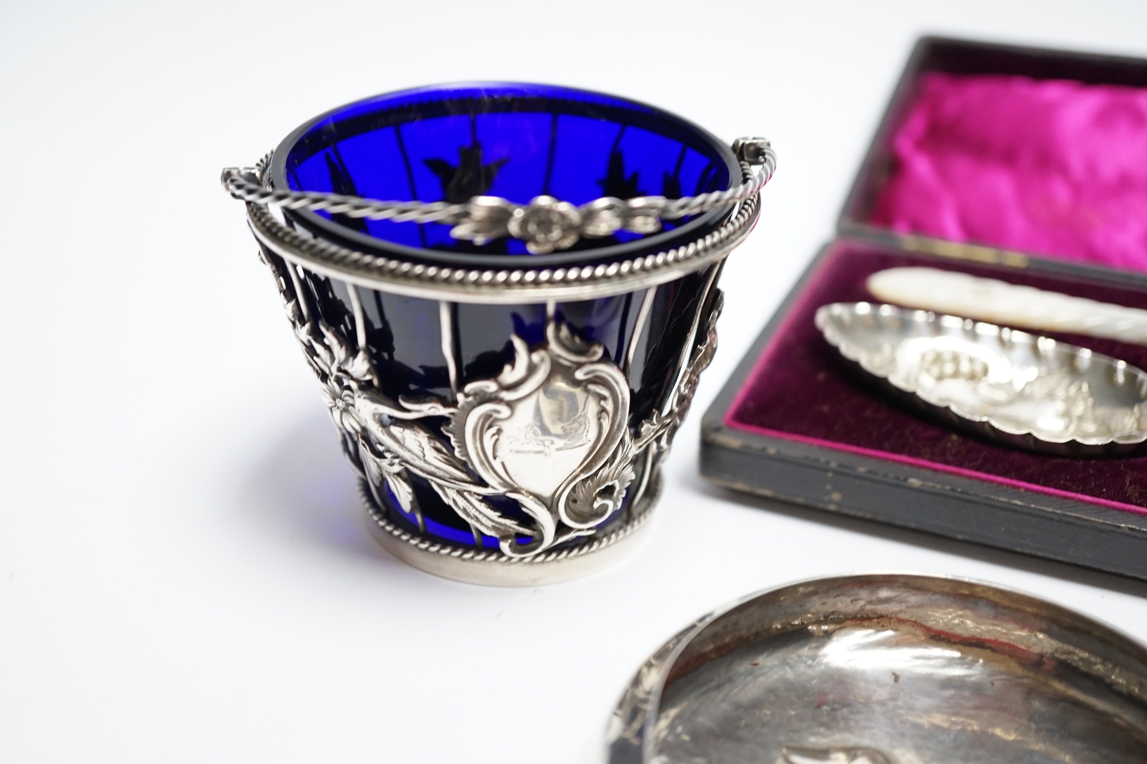 A cased pair of late Victorian mother of pearl handled silver 'berry' spoons, by A.J. Bailey, Birmingham, 1896, a continental white metal spoon with figural terminal, a pierced white metal sugar basket, with blue glass l